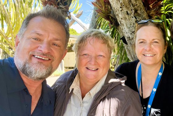 Three people, from the shoulders up, outdoors and smiling at the camera.